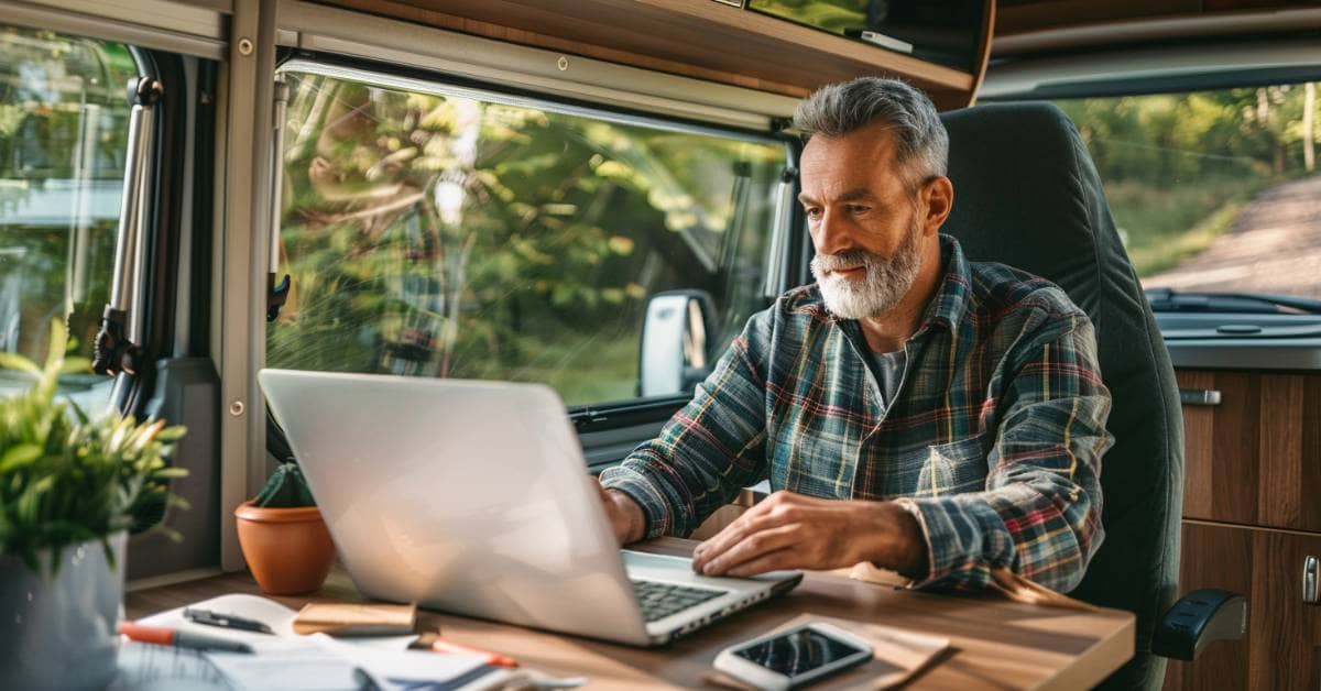 Middle-aged man working on a laptop inside a motorhome, focused and engaged in his affiliate marketing work, with a cozy and minimalistic interior